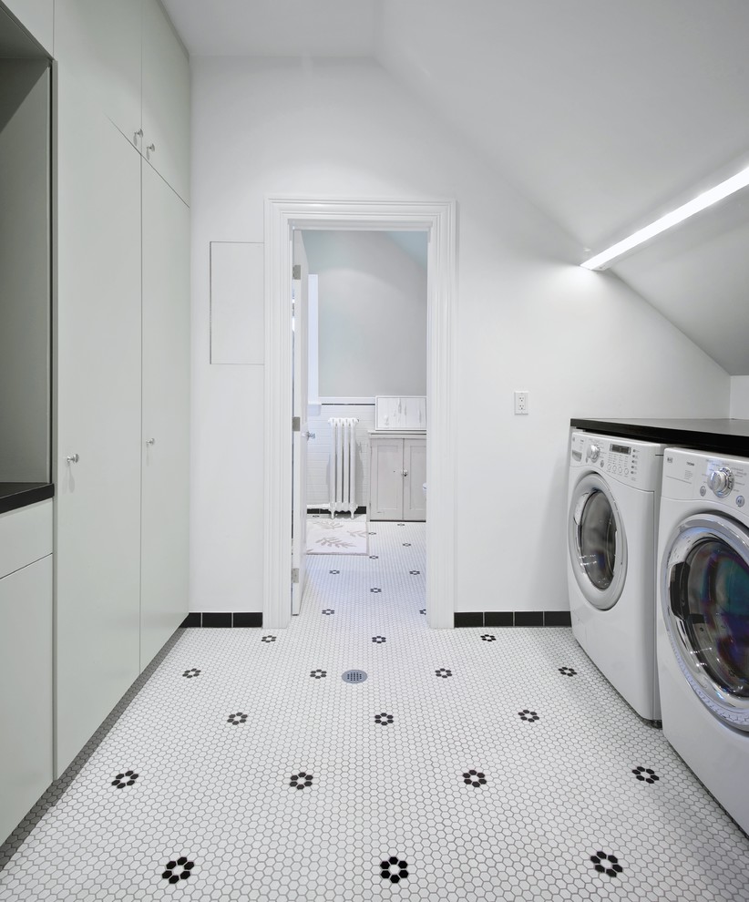 トロントにある高級な中くらいな北欧スタイルのおしゃれな洗濯室 (ll型、フラットパネル扉のキャビネット、グレーのキャビネット、クオーツストーンカウンター、白い壁、左右配置の洗濯機・乾燥機、磁器タイルの床、白い床、黒いキッチンカウンター) の写真
