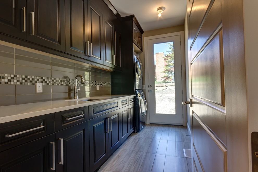 This is an example of a medium sized contemporary single-wall utility room in Calgary with a submerged sink, raised-panel cabinets, dark wood cabinets, composite countertops, brown walls, porcelain flooring, a stacked washer and dryer and grey floors.