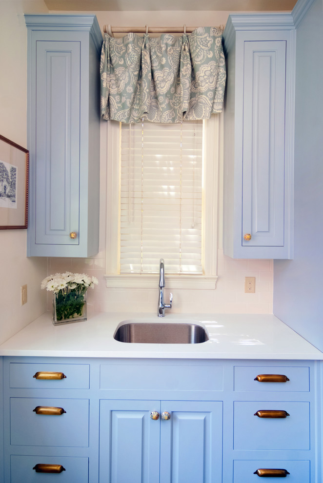 Inredning av en klassisk mellanstor vita parallell vitt tvättstuga enbart för tvätt, med en undermonterad diskho, luckor med upphöjd panel, blå skåp, bänkskiva i kvarts, vita väggar, en tvättmaskin och torktumlare bredvid varandra, tegelgolv och brunt golv