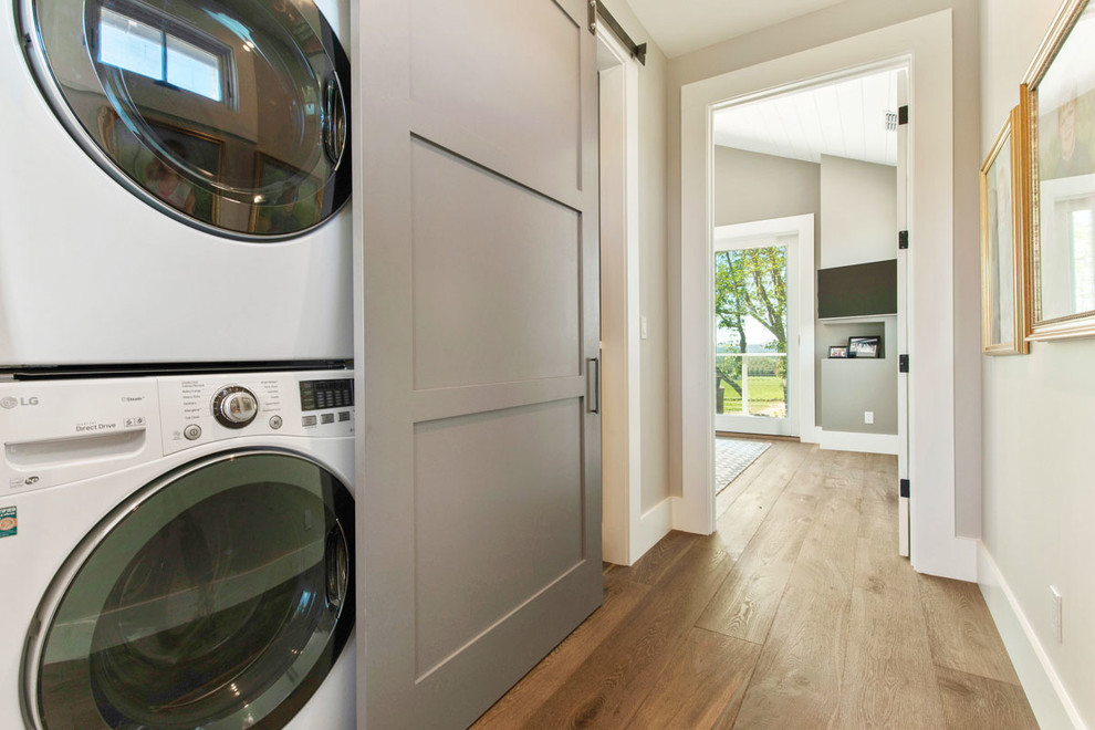 Imagen de armario lavadero lineal de estilo de casa de campo pequeño con suelo de madera oscura y lavadora y secadora apiladas