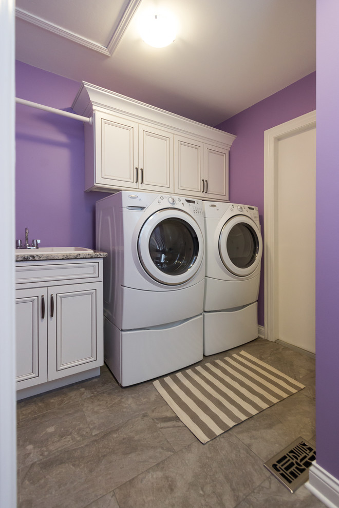 Idéer för att renovera en mellanstor vintage linjär tvättstuga enbart för tvätt, med en allbänk, luckor med infälld panel, vita skåp, granitbänkskiva, lila väggar, klinkergolv i porslin, en tvättmaskin och torktumlare bredvid varandra och beiget golv
