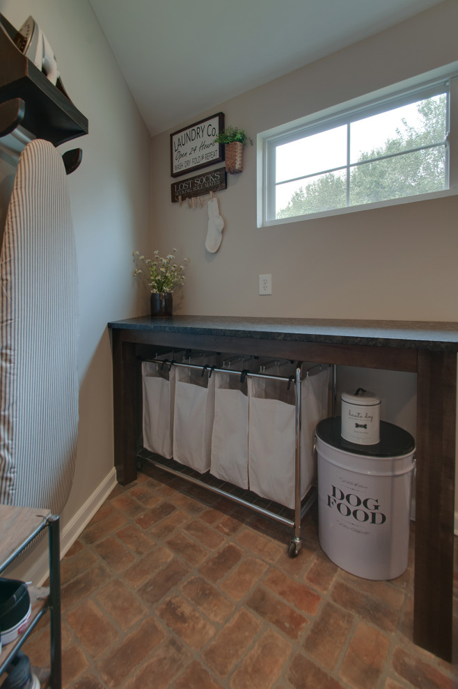 Example of a small cottage brick floor and multicolored floor utility room design in Nashville with a farmhouse sink, shaker cabinets, brown cabinets, granite countertops, gray walls, a side-by-side washer/dryer and black countertops