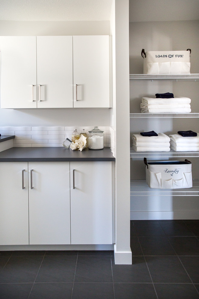 Medium sized contemporary galley separated utility room in Calgary with flat-panel cabinets, white cabinets, engineered stone countertops, white walls, ceramic flooring, a side by side washer and dryer and grey floors.