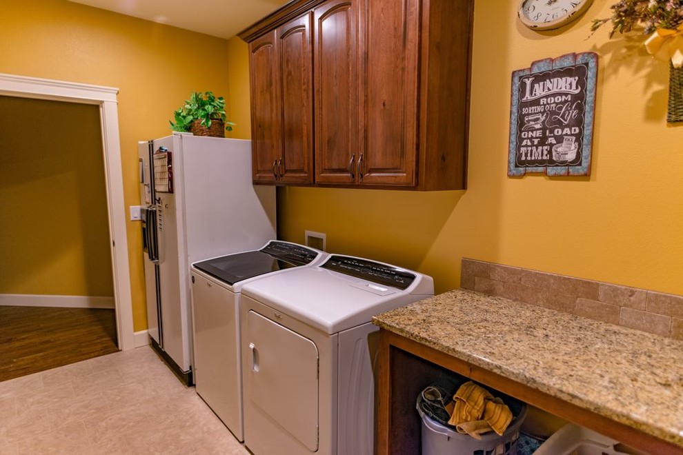 Esempio di una grande sala lavanderia con ante con bugna sagomata, ante marroni, top in granito, pareti gialle, lavatrice e asciugatrice affiancate, pavimento beige e top multicolore