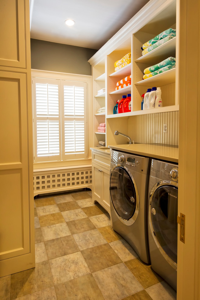 Modelo de cuarto de lavado lineal clásico con armarios abiertos, puertas de armario beige, paredes beige, lavadora y secadora juntas y encimeras beige
