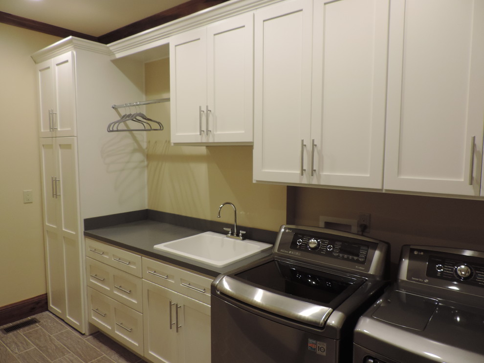Example of a mid-sized trendy single-wall porcelain tile dedicated laundry room design in Kansas City with a drop-in sink, shaker cabinets, white cabinets, solid surface countertops, a side-by-side washer/dryer and beige walls