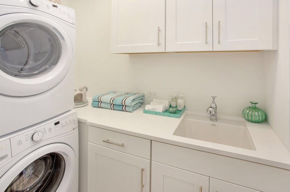 Modelo de cuarto de lavado marinero pequeño con fregadero bajoencimera, paredes blancas y lavadora y secadora apiladas