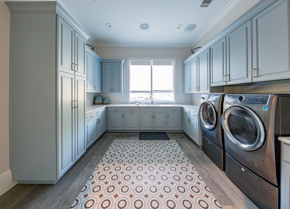 Idéer för en mycket stor klassisk u-formad tvättstuga enbart för tvätt, med en undermonterad diskho, luckor med upphöjd panel, grå skåp, bänkskiva i kvarts, beige väggar, mellanmörkt trägolv, en tvättmaskin och torktumlare bredvid varandra och grått golv