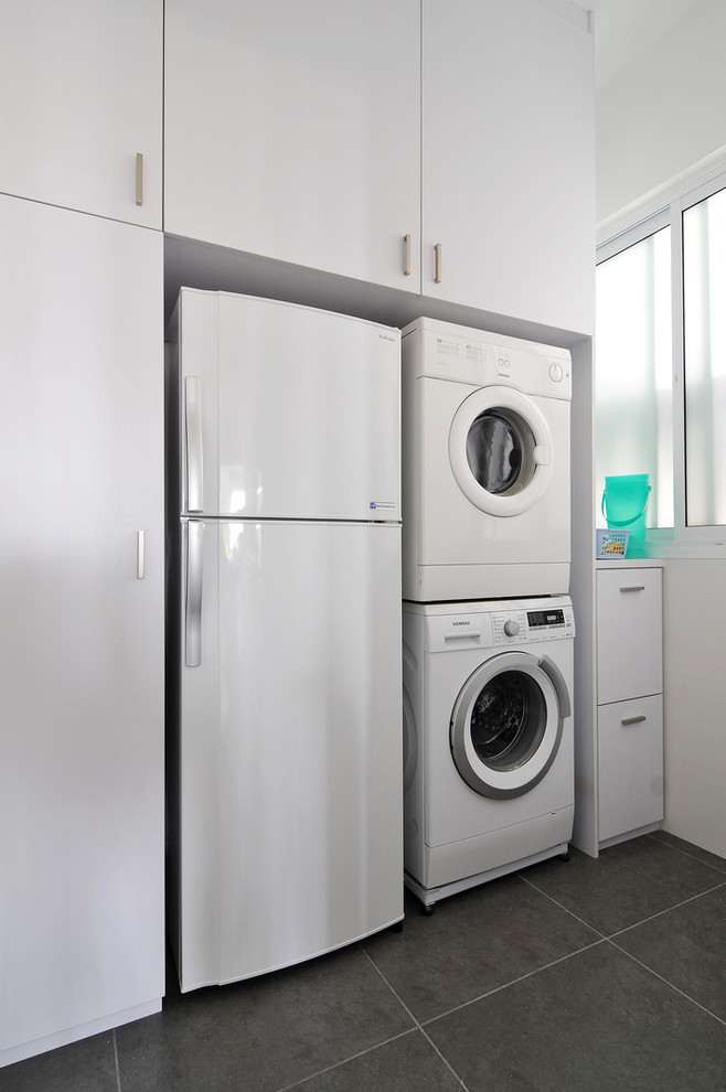 Modelo de lavadero lineal y multiusos contemporáneo con armarios con paneles lisos, puertas de armario blancas, paredes blancas y lavadora y secadora apiladas