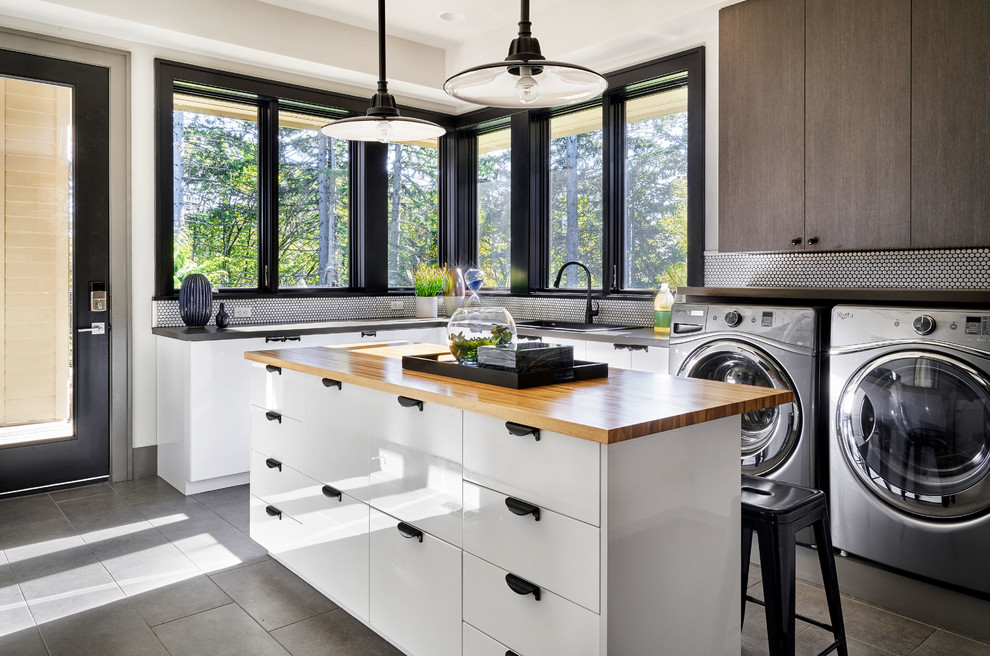 This is an example of a large contemporary u-shaped utility room in Portland with a built-in sink, flat-panel cabinets, white cabinets, wood worktops, grey walls, porcelain flooring, a side by side washer and dryer and grey floors.