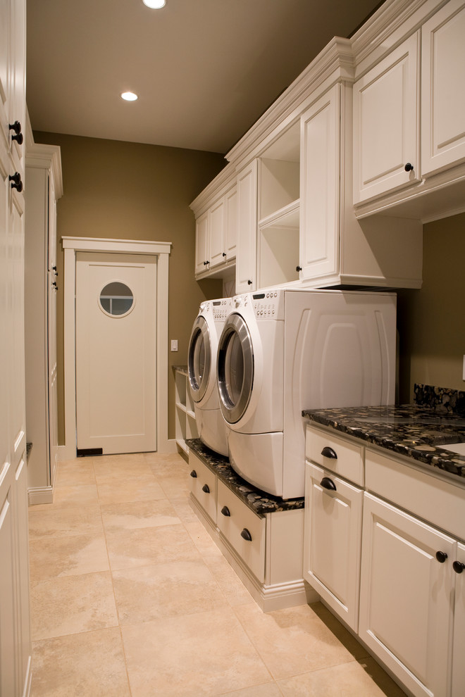Bild på ett amerikanskt parallellt grovkök, med vita skåp, granitbänkskiva, klinkergolv i porslin och en tvättmaskin och torktumlare bredvid varandra