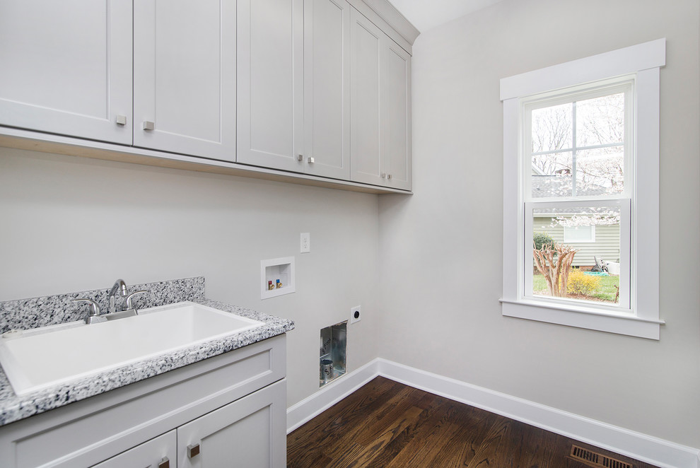 Design ideas for a classic single-wall utility room in Charlotte with a built-in sink, recessed-panel cabinets, grey cabinets, granite worktops, grey walls, dark hardwood flooring and a side by side washer and dryer.