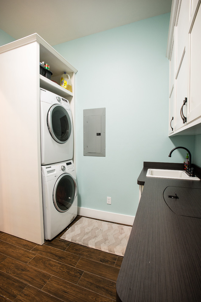 Immagine di una lavanderia multiuso stile americano di medie dimensioni con lavello da incasso, ante bianche, pareti blu, pavimento in legno massello medio, lavatrice e asciugatrice a colonna e pavimento marrone
