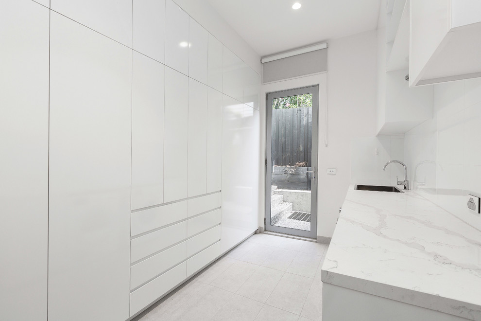 Exempel på en stor modern vita parallell vitt tvättstuga enbart för tvätt, med vita skåp, marmorbänkskiva, vita väggar, klinkergolv i porslin, en tvättmaskin och torktumlare bredvid varandra och grått golv