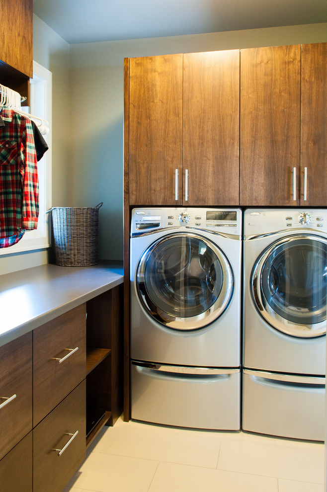 Ejemplo de lavadero actual con armarios con paneles lisos, lavadora y secadora juntas y puertas de armario de madera en tonos medios
