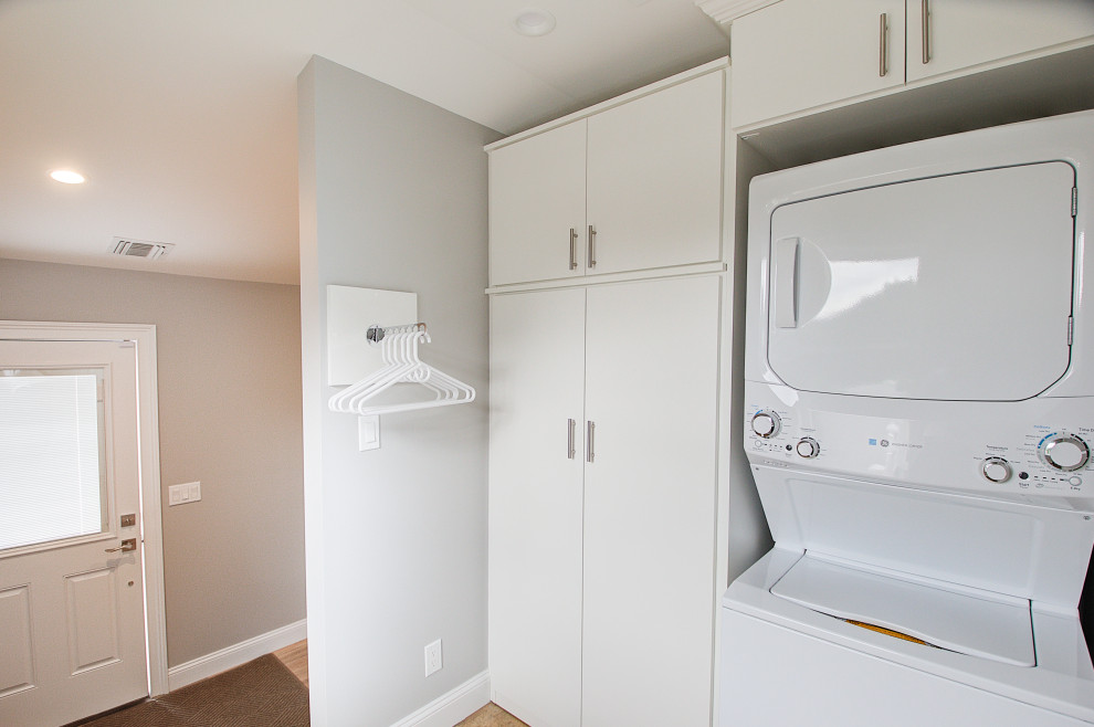 Zweizeilige, Mittelgroße Klassische Waschküche mit flächenbündigen Schrankfronten, weißen Schränken, grauer Wandfarbe, Porzellan-Bodenfliesen, Waschmaschine und Trockner gestapelt und beigem Boden in New York