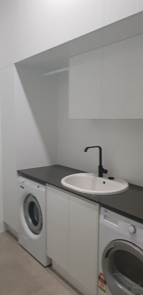 Minimalist porcelain tile and gray floor laundry room photo in Brisbane with a drop-in sink, white cabinets, quartz countertops, white walls, a side-by-side washer/dryer and brown countertops