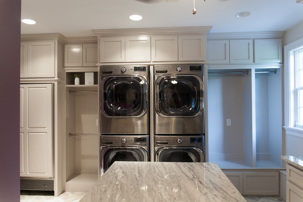 This is an example of a large traditional separated utility room in New Orleans with a belfast sink, shaker cabinets, grey cabinets, granite worktops, white walls, porcelain flooring and a stacked washer and dryer.