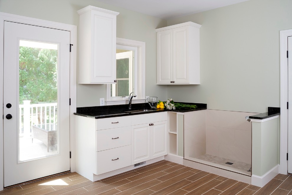 Idéer för en mellanstor klassisk l-formad tvättstuga enbart för tvätt, med luckor med upphöjd panel, vita skåp, vinylgolv, brunt golv, granitbänkskiva, grå väggar och en undermonterad diskho