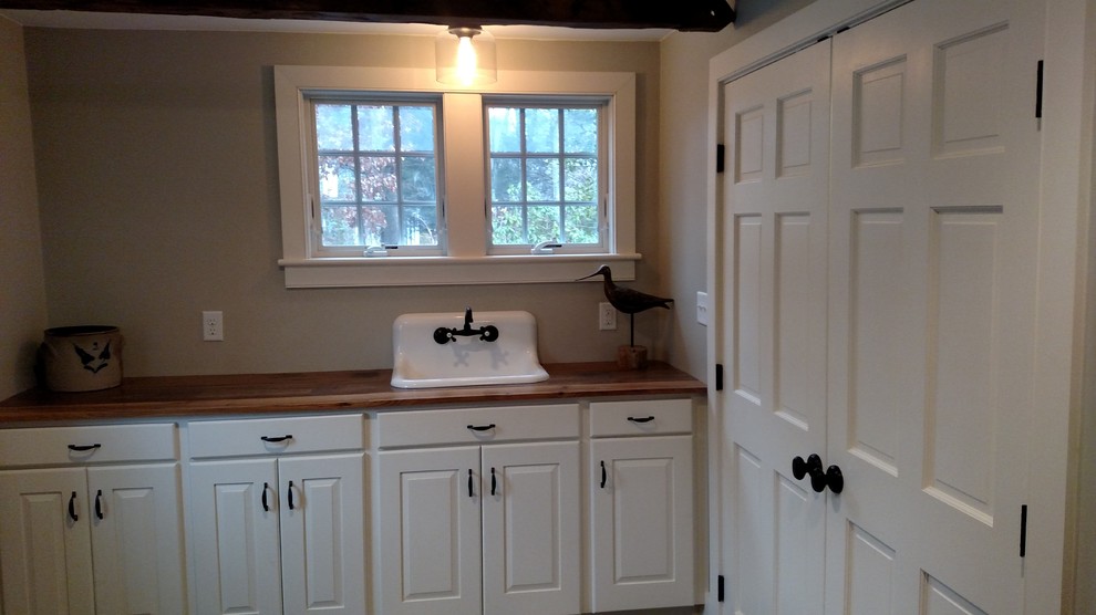 Immagine di una sala lavanderia country con lavello stile country, ante in stile shaker, ante bianche, top in legno, pavimento in vinile e lavatrice e asciugatrice nascoste