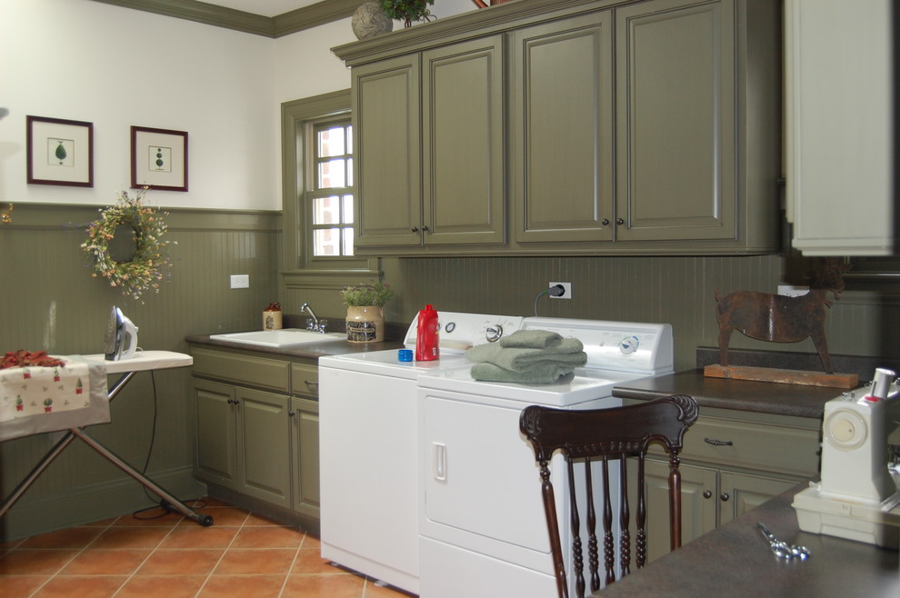 Foto på en vintage tvättstuga, med en nedsänkt diskho, luckor med upphöjd panel, gröna skåp, en tvättmaskin och torktumlare bredvid varandra, klinkergolv i terrakotta, rött golv och vita väggar