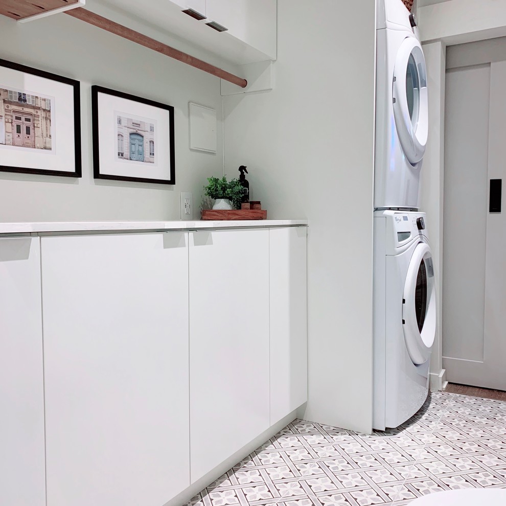 Bild på en vita parallell vitt tvättstuga, med släta luckor, vita skåp, bänkskiva i kvarts, vita väggar, klinkergolv i porslin och en tvättpelare