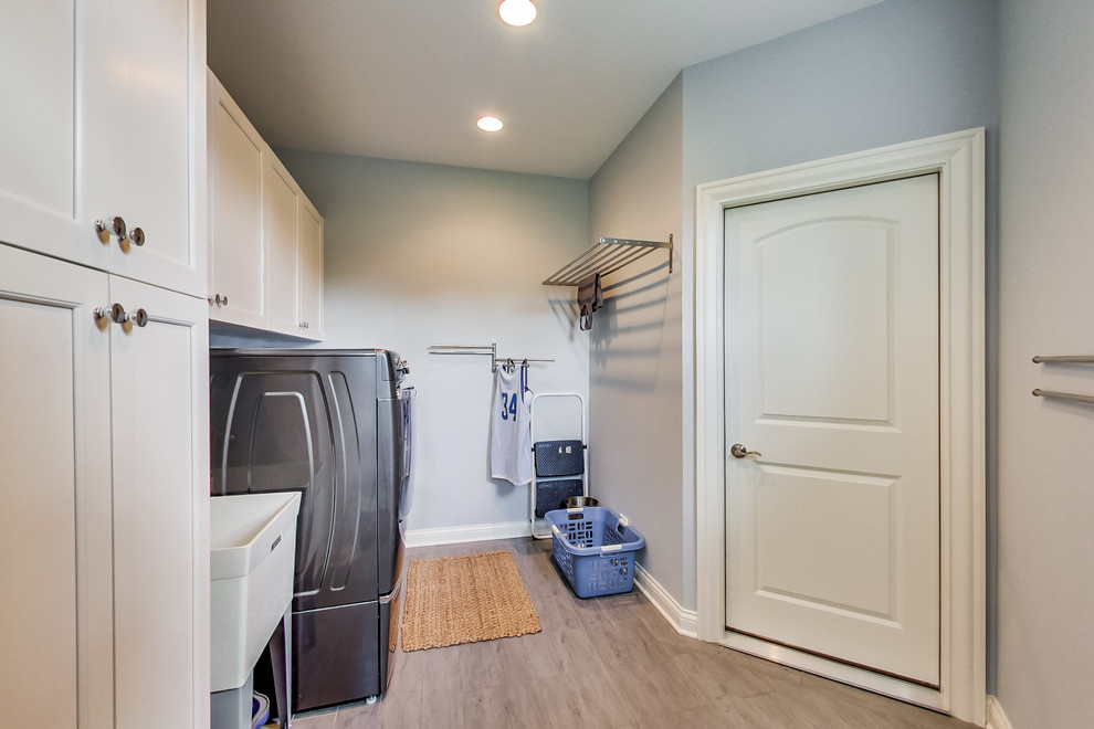 Design ideas for an expansive classic single-wall separated utility room in Chicago with an utility sink, shaker cabinets, white cabinets, grey walls, dark hardwood flooring, a side by side washer and dryer and beige floors.