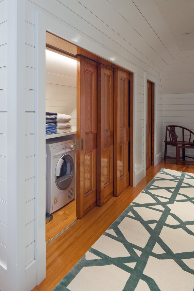 Foto di un ripostiglio-lavanderia stile marino di medie dimensioni con pareti bianche, pavimento in legno massello medio e lavatrice e asciugatrice affiancate