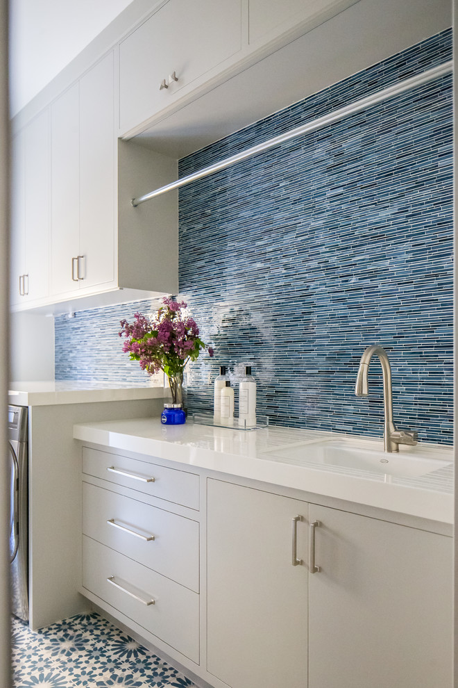 Idéer för stora medelhavsstil parallella vitt tvättstugor enbart för tvätt, med en undermonterad diskho, släta luckor, grå skåp, blå väggar, en tvättmaskin och torktumlare bredvid varandra och blått golv