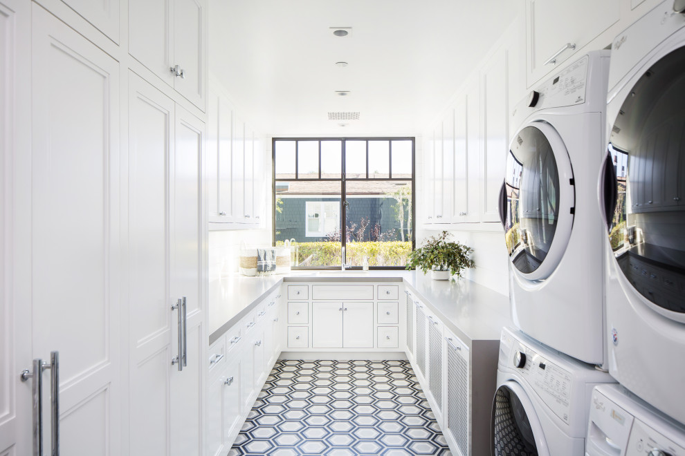 Esempio di un'ampia sala lavanderia stile marino con lavello da incasso, ante con riquadro incassato, ante bianche, pareti bianche, lavatrice e asciugatrice a colonna e top grigio
