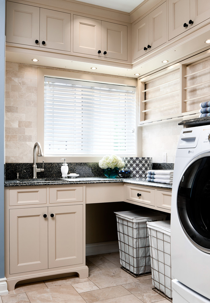 Modelo de lavadero multiusos clásico grande con fregadero bajoencimera, puertas de armario beige, paredes beige y lavadora y secadora juntas