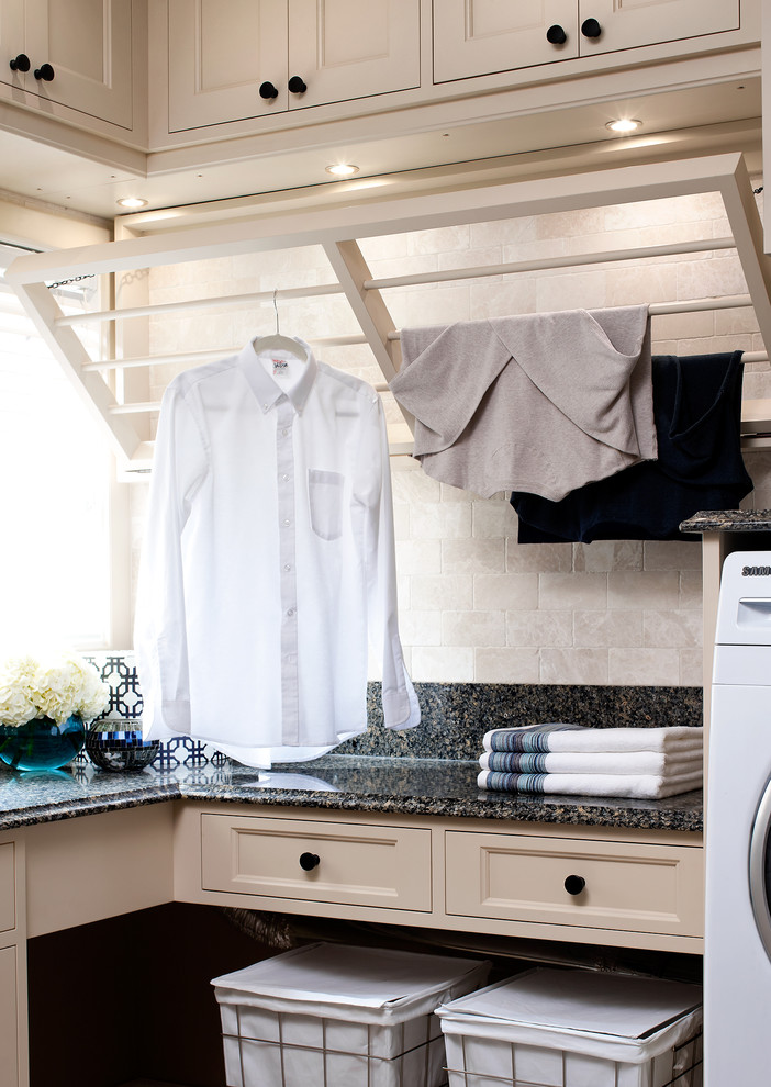 Imagen de lavadero clásico con puertas de armario beige, armarios con paneles empotrados y encimeras negras