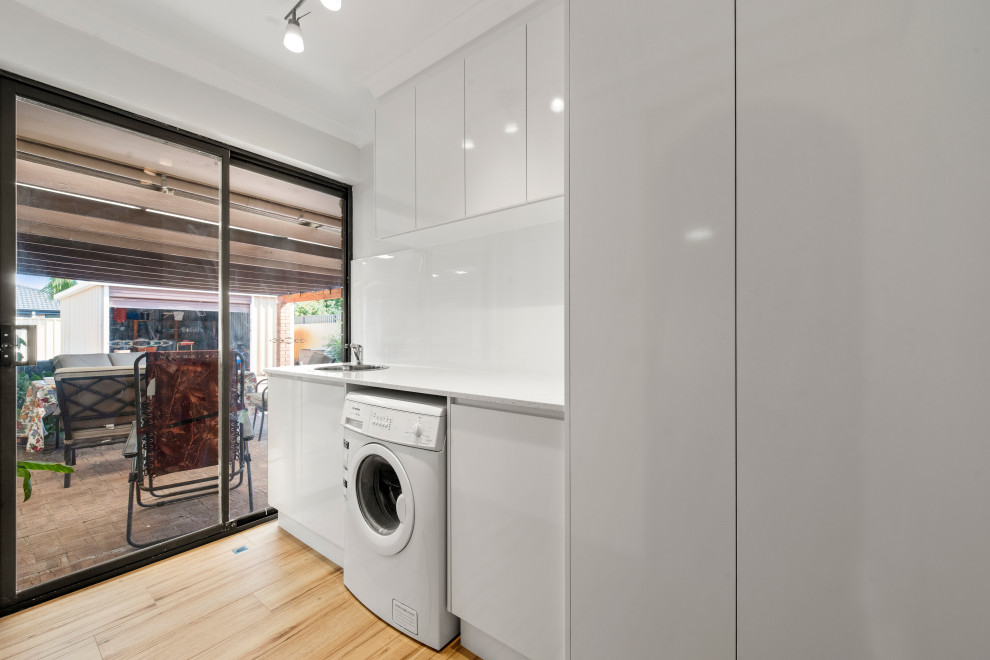 Immagine di una sala lavanderia moderna di medie dimensioni con lavello da incasso, ante in stile shaker, ante bianche, pareti bianche, pavimento giallo e top bianco