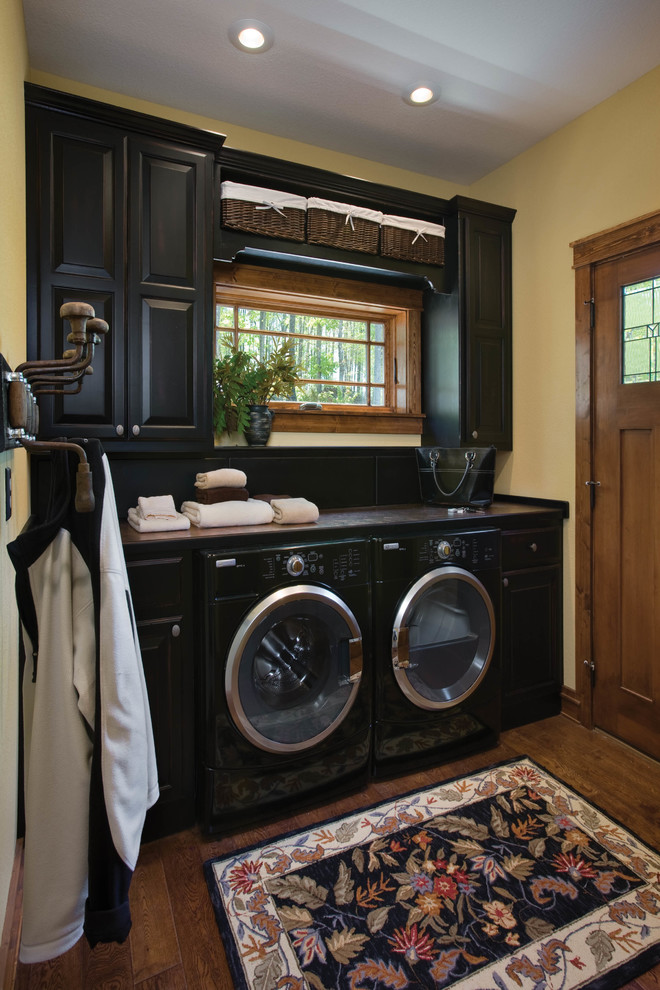 Dedicated laundry room - mid-sized rustic single-wall dark wood floor dedicated laundry room idea in Other with black cabinets, beige walls, raised-panel cabinets and a side-by-side washer/dryer