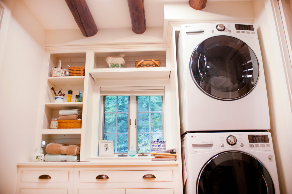 Diseño de cuarto de lavado lineal rústico de tamaño medio con armarios estilo shaker, puertas de armario blancas, encimera de madera, paredes blancas y lavadora y secadora apiladas