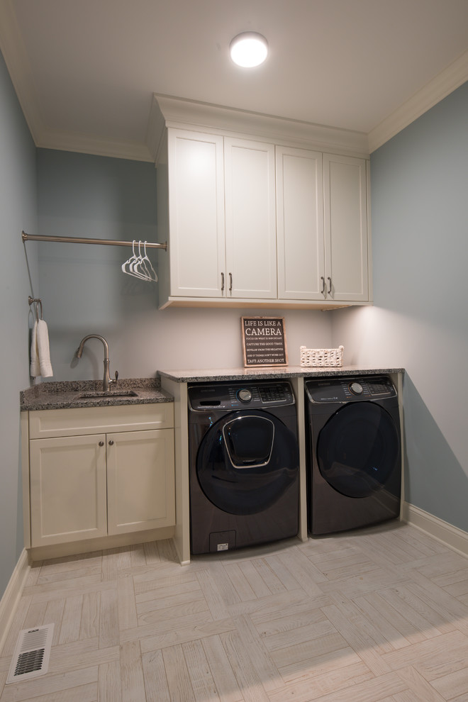 Klassisk inredning av en mellanstor linjär tvättstuga enbart för tvätt, med en undermonterad diskho, luckor med infälld panel, vita skåp, granitbänkskiva, klinkergolv i keramik, en tvättmaskin och torktumlare bredvid varandra, beiget golv och grå väggar