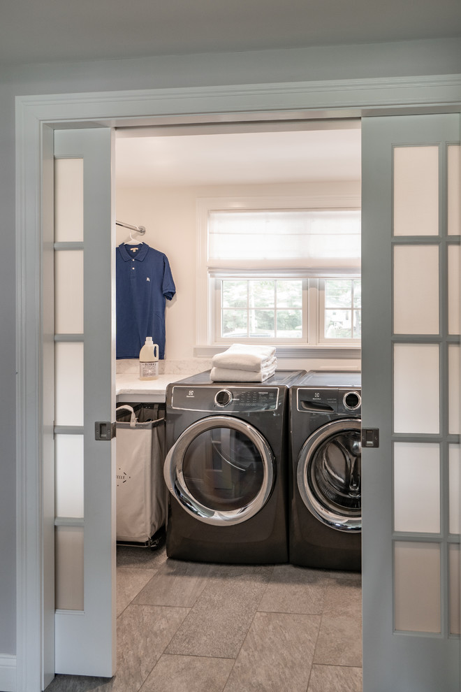 Large transitional u-shaped porcelain tile and gray floor dedicated laundry room photo in Boston with white walls, a side-by-side washer/dryer, white countertops, shaker cabinets, white cabinets and quartz countertops