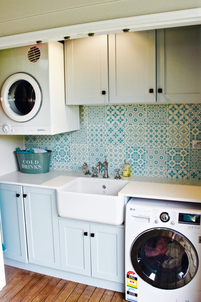 Lantlig inredning av en linjär liten tvättstuga, med skåp i shakerstil, blå skåp, blå väggar och en rustik diskho