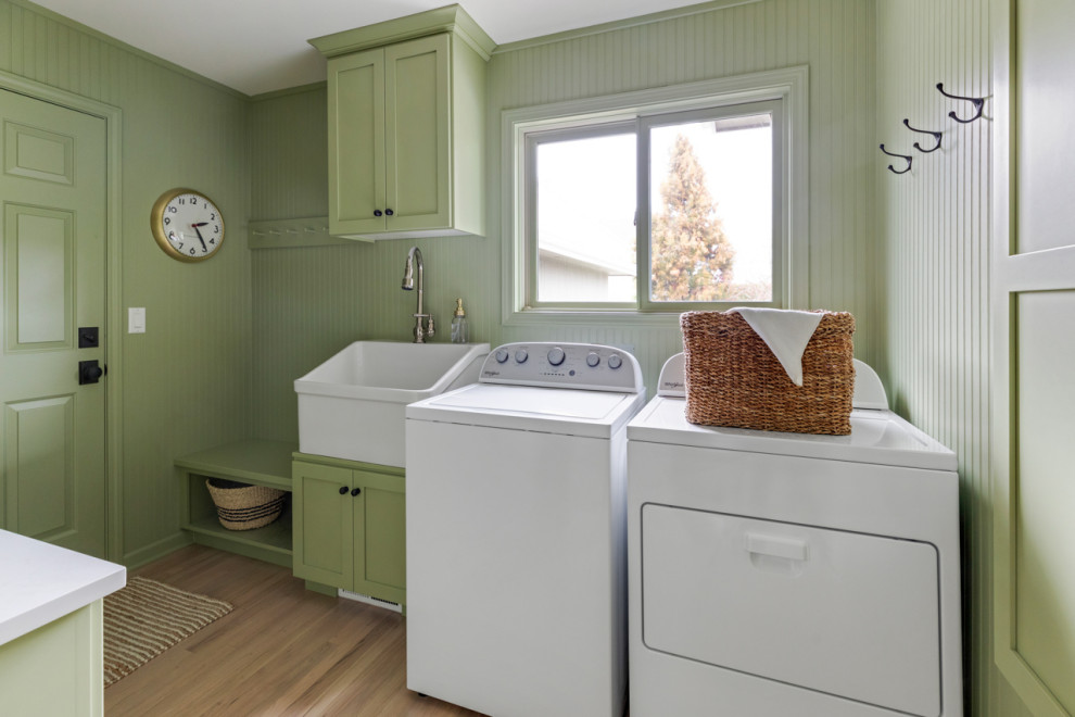 Inredning av en lantlig mycket stor vita parallell vitt tvättstuga enbart för tvätt, med en rustik diskho, skåp i shakerstil, gröna skåp, bänkskiva i kvartsit, gröna väggar, ljust trägolv och en tvättmaskin och torktumlare bredvid varandra