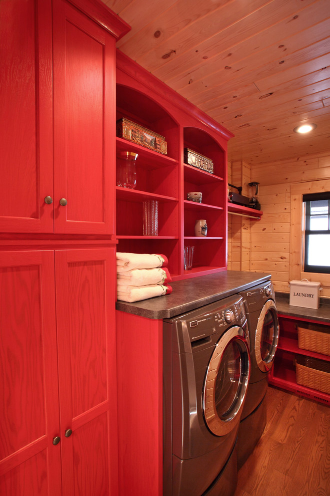 Esempio di una sala lavanderia stile rurale di medie dimensioni con ante lisce, ante rosse, top in laminato, pareti marroni, pavimento in legno massello medio e lavatrice e asciugatrice affiancate