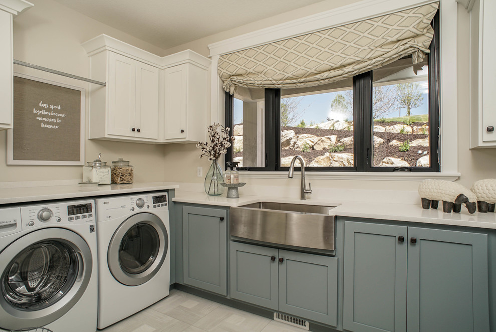 Laundry room - farmhouse gray floor laundry room idea in Salt Lake City with a farmhouse sink, shaker cabinets, blue cabinets, beige walls, a side-by-side washer/dryer and white countertops
