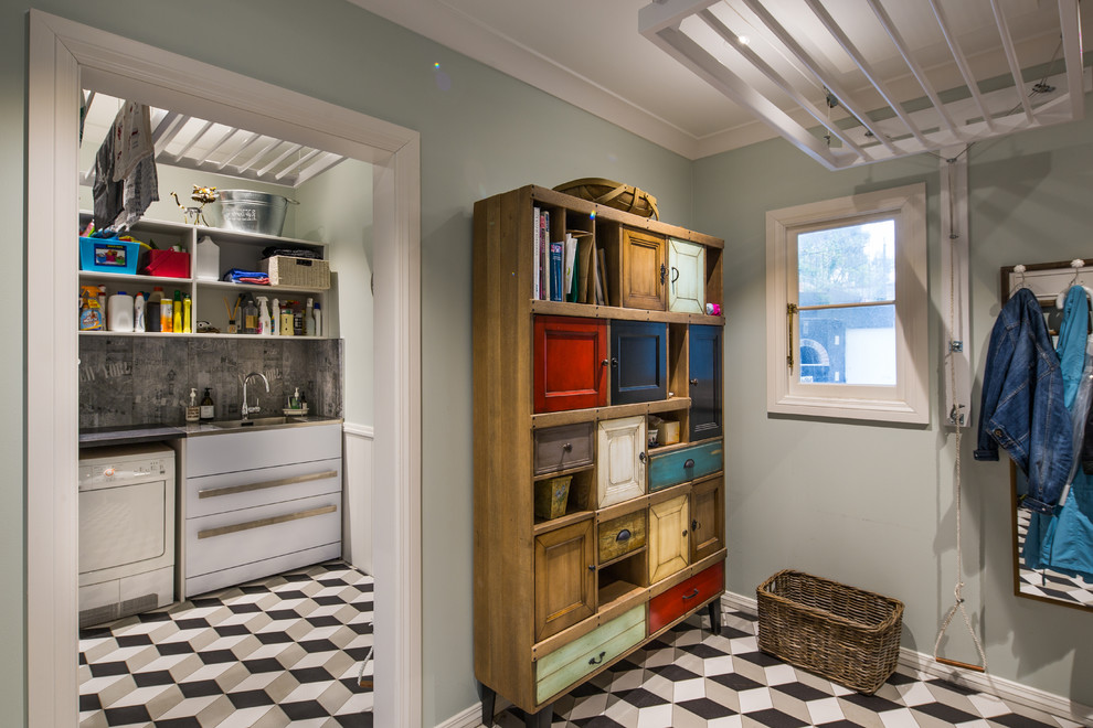 ウェリントンにある高級な広いヴィクトリアン調のおしゃれな洗濯室 (スロップシンク、御影石カウンター、青い壁、磁器タイルの床、左右配置の洗濯機・乾燥機) の写真
