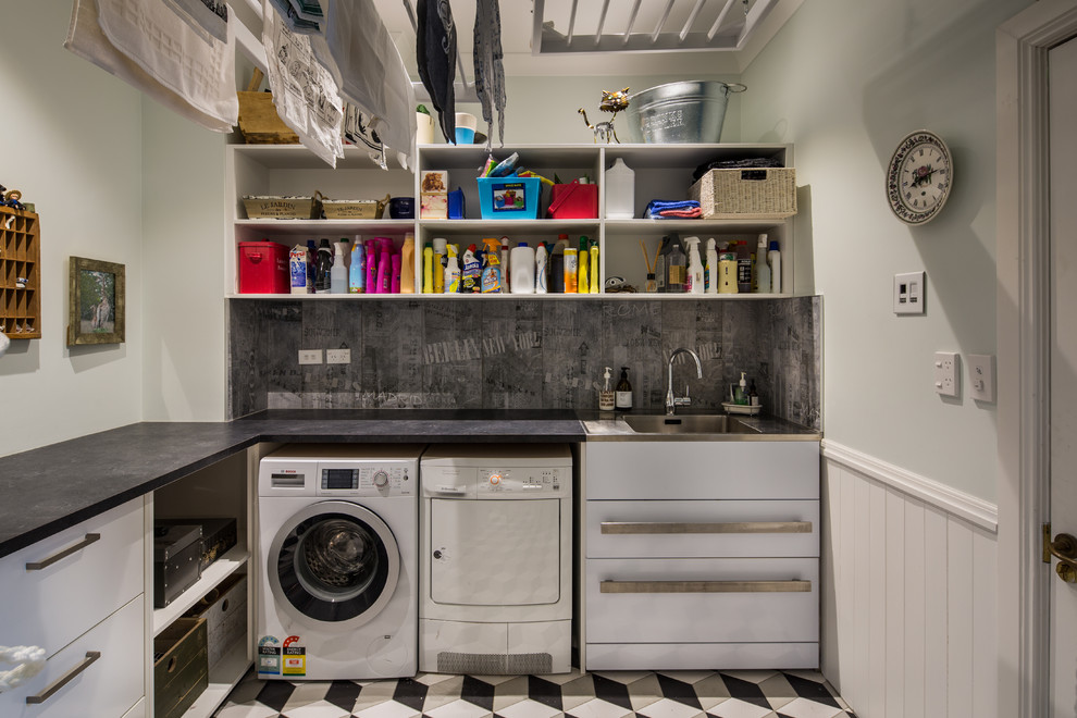 ウェリントンにある高級な広いヴィクトリアン調のおしゃれな洗濯室 (スロップシンク、御影石カウンター、青い壁、磁器タイルの床、左右配置の洗濯機・乾燥機) の写真