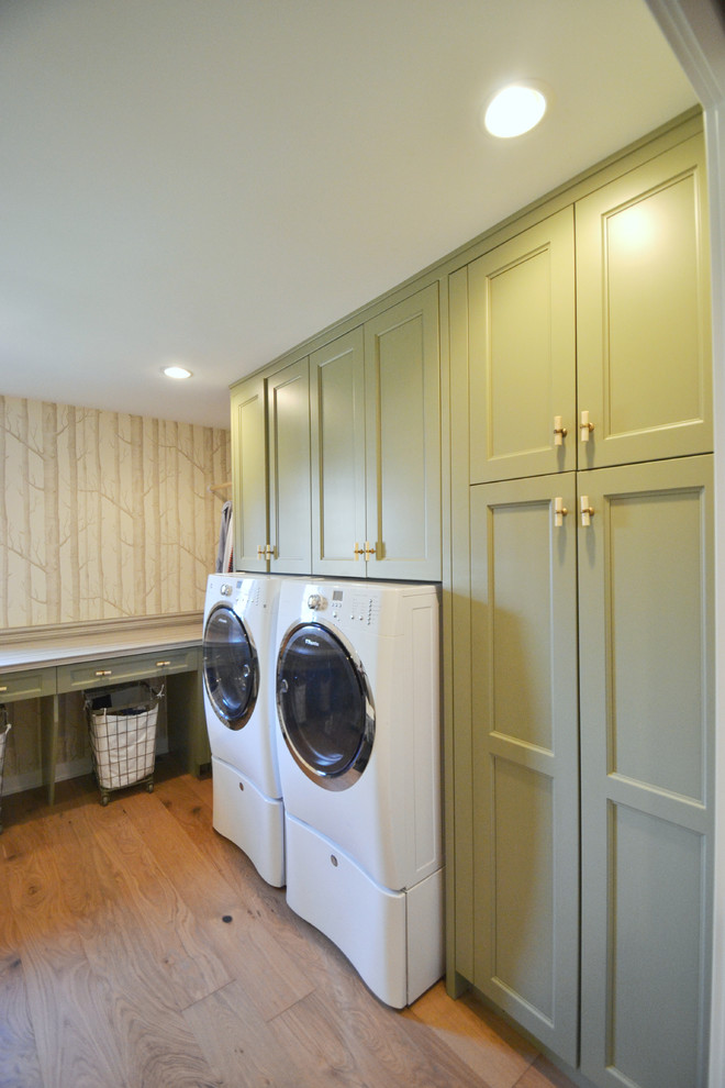 Inredning av en modern mellanstor l-formad tvättstuga enbart för tvätt, med luckor med infälld panel, gröna skåp, vita väggar, ljust trägolv och en tvättmaskin och torktumlare bredvid varandra