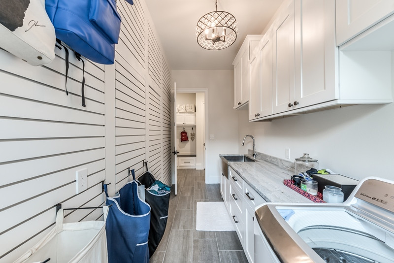 Large country galley separated utility room in Houston with a belfast sink, shaker cabinets, white cabinets, granite worktops, white walls, porcelain flooring, a side by side washer and dryer, grey floors and grey worktops.