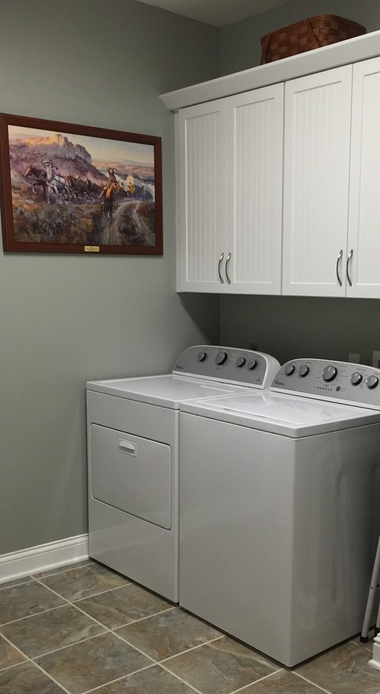 Exempel på en liten klassisk tvättstuga enbart för tvätt, med luckor med infälld panel, vita skåp, gröna väggar och en tvättmaskin och torktumlare bredvid varandra