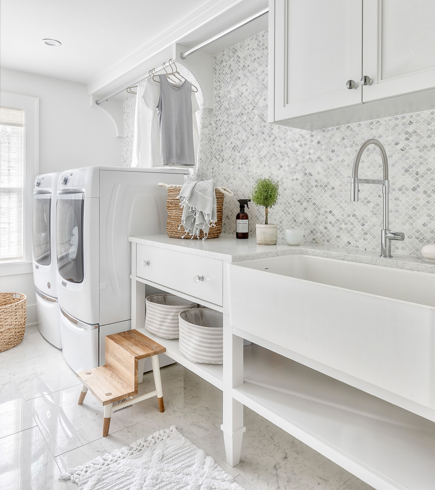 Exempel på en klassisk vita vitt tvättstuga enbart för tvätt, med en allbänk, luckor med infälld panel, vita skåp, vita väggar, en tvättmaskin och torktumlare bredvid varandra och vitt golv