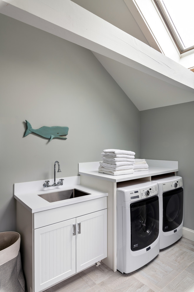 Example of a beach style single-wall beige floor dedicated laundry room design in Boston with a single-bowl sink, recessed-panel cabinets, white cabinets, gray walls, a side-by-side washer/dryer and white countertops