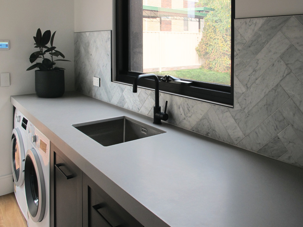 Photo of a medium sized modern single-wall separated utility room in Other with a submerged sink, shaker cabinets, black cabinets, engineered stone countertops, grey walls, medium hardwood flooring, a side by side washer and dryer, brown floors and grey worktops.