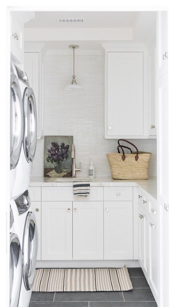 Ejemplo de cuarto de lavado en L costero pequeño con encimera de mármol, paredes blancas, lavadora y secadora apiladas, suelo gris y encimeras blancas